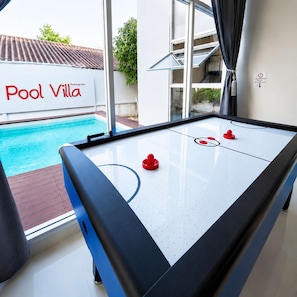 A pool table with a clear view of a swimming pool outside, a sign reading 'Pool Villa', and a window with curtains. - 3-Bedroom Private Pool Villa for Up to 10 Guests (Si Racha)