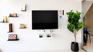 Un saló modern amb un televisor de pantalla plana fixat a la paret, envoltat d'estanteries amb llibres i objectes decoratius, una planta en test i una porta visible que dona a una altra estança.