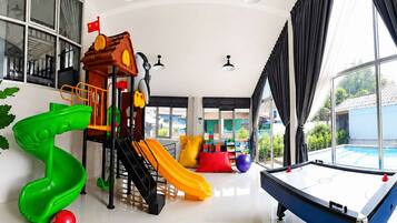 Un espacio interior amplio con zona de juegos para niños, mesa de billar y grandes ventanales que ofrecen vistas al exterior.