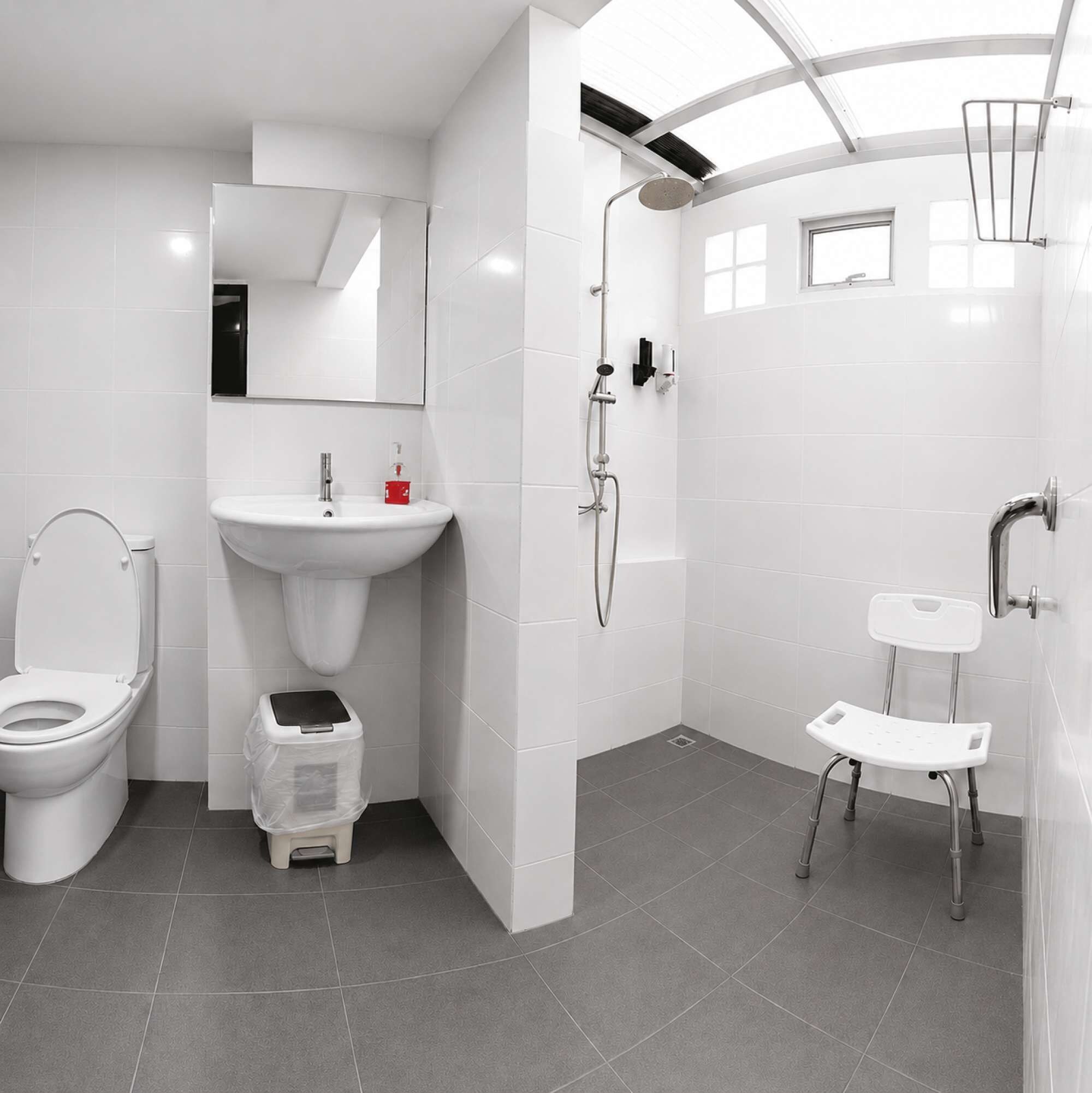 Ein modernes Badezimmer mit Toilette, Waschbecken, Dusche und einer kleinen Stehgehocker.