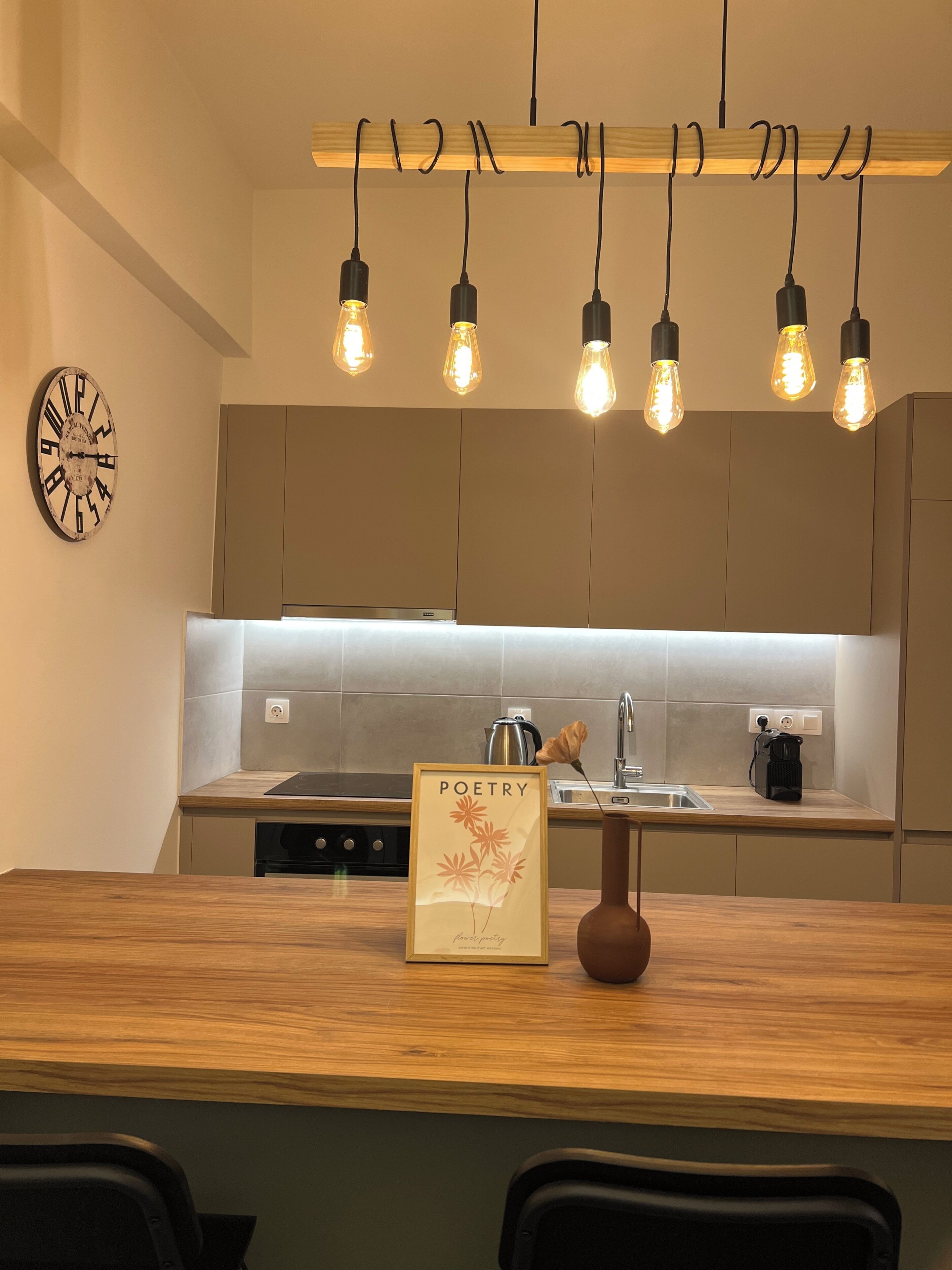 A modern kitchen with a wooden countertop, a clock, and a book titled 'POETRY' on the counter.