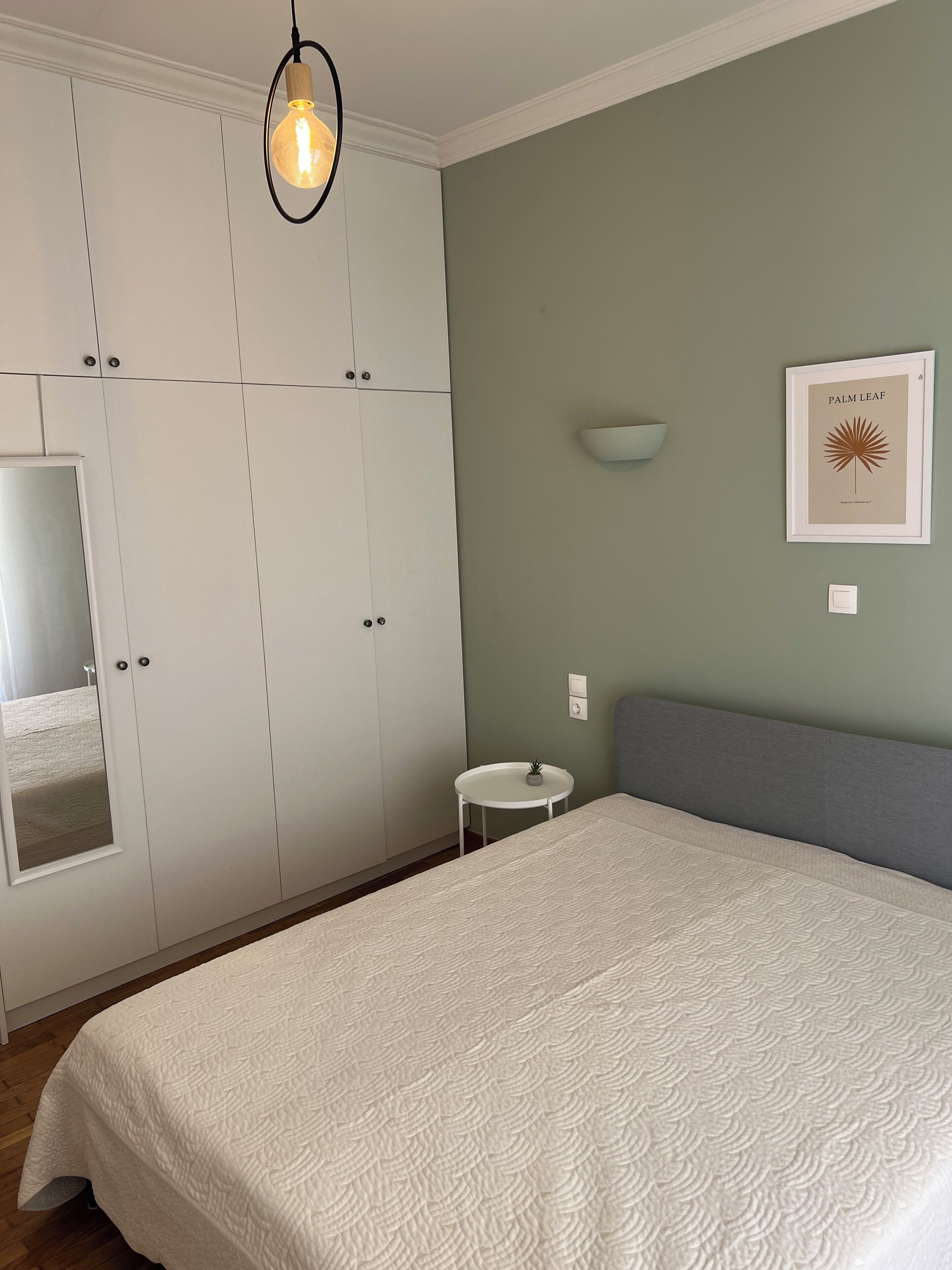 Een slaapkamer met een bed, kast, nachtkastje, lamp en een lijst met een afbeelding aan de muur.