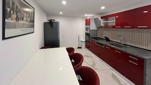 A modern kitchen with red cabinets, a white countertop, and a dining area with a white table and red chairs.