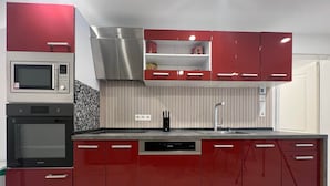 A modern kitchen with built-in appliances, a stainless steel range hood, and red cabinetry.
