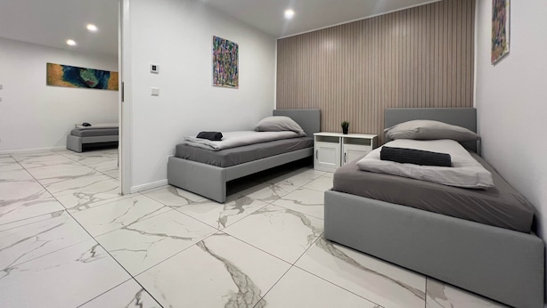 A modern bedroom with two beds, a small bedside table, a mirror, and a wall-mounted artwork.