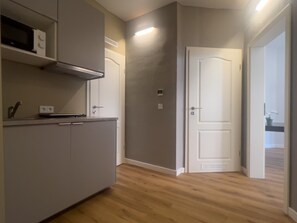 Una cocina con armarios, un microondas y una estufa. Se ve una puerta con manija e interruptor de luz en la pared.