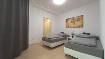 Una habitación con dos camas, una mesita con una planta, un mapa del mundo en la pared y una puerta que da a otra habitación.