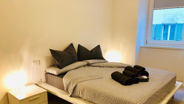 Ein Bett mit gestreifter Bettdecke, zwei Kissen und zusammengerollten Handtüchern auf einem weißen Nachttisch.