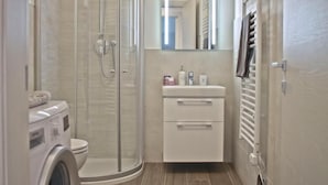 Ein Badezimmer mit Duschkabine, Toilette, Waschbecken mit Spiegel und Handtuchhalter.