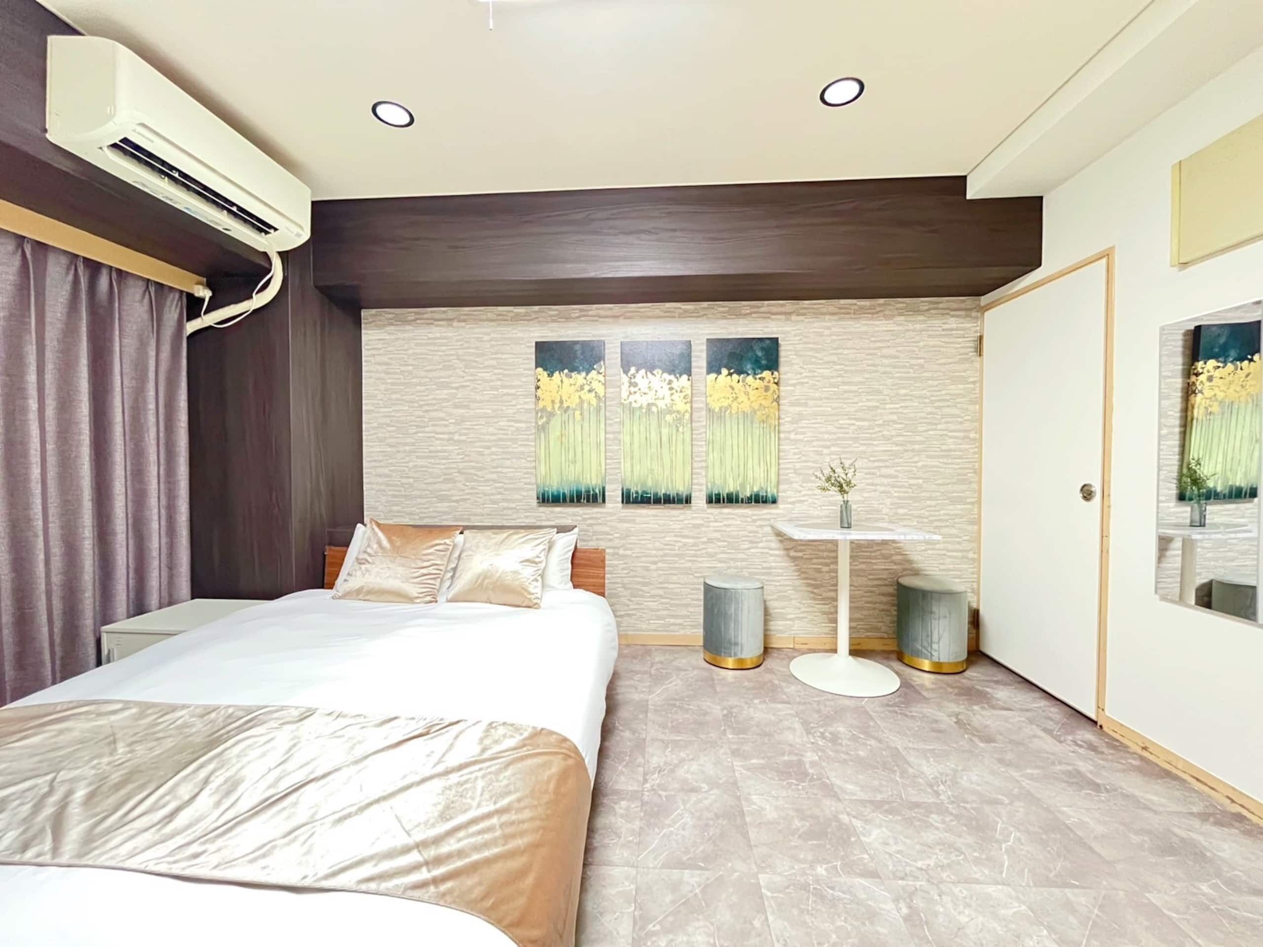 Une chambre moderne équipée d’un lit, d’un climatiseur, d’œuvres d’art, d’une petite table et d’une porte.