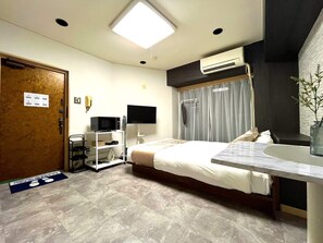 Ein Hotelzimmer mit Bett, Nachttisch, Fernseher, Klimaanlage und Schreibtisch mit Stuhl.