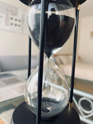 An hourglass with a clear glass structure, supported by black stands, placed on a surface with a cord and papers in the background. - Wonderful Studio, Geneva perfect for your city getaway (Genève)