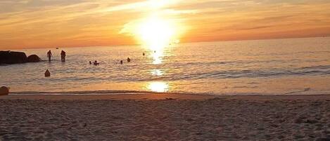 Ein Strand mit Dünen und einem Sonnenuntergang über dem Wasser.