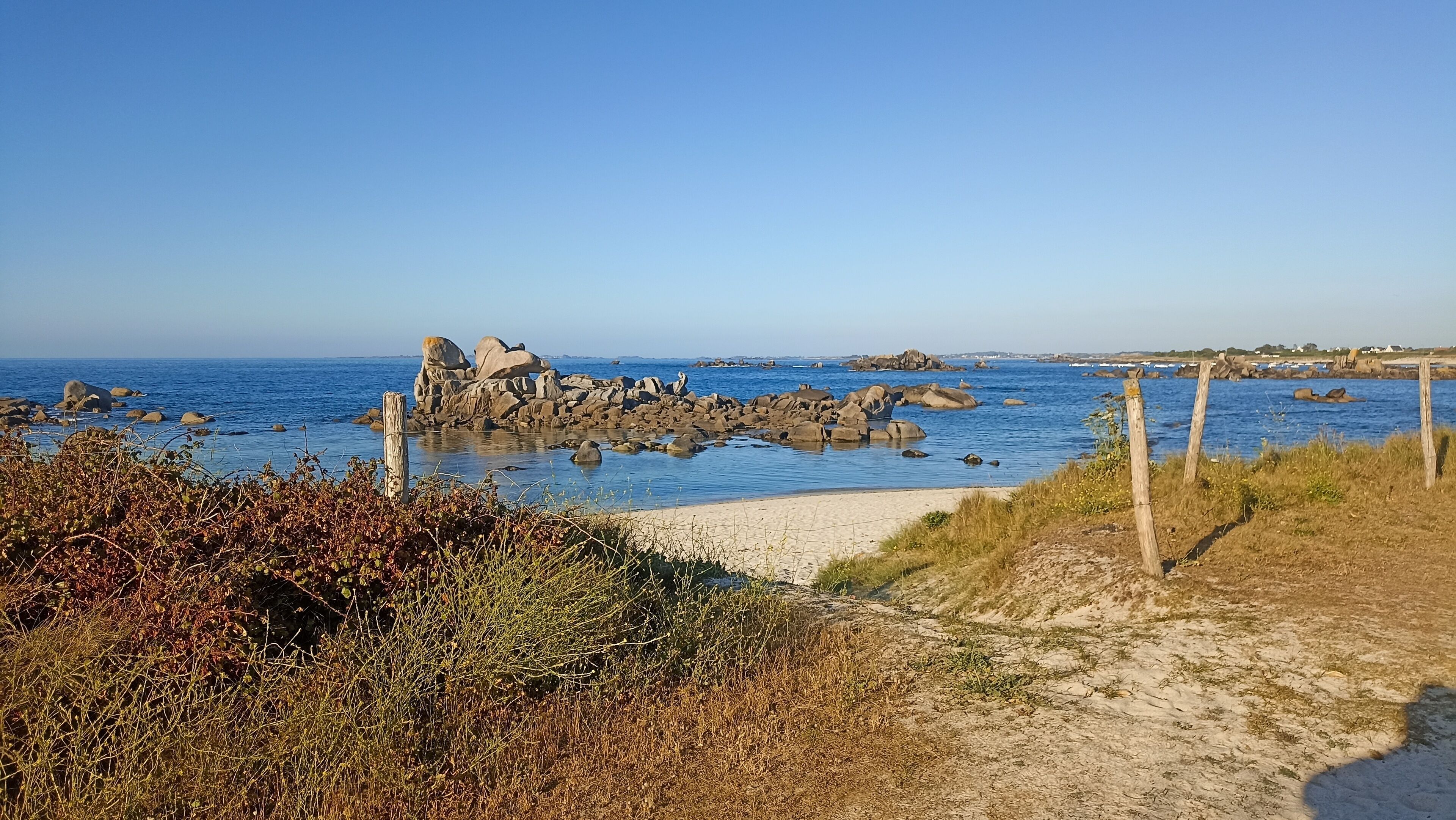 Et kystlandskab med en sandsti, der fører ned til havet, omgivet af klippeformationer og vegetation.