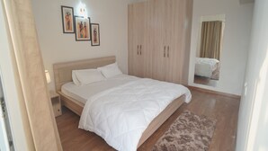 Ein Schlafzimmer mit einem Bett, einem Holzschrank, einem Nachttisch und einem an der Wand befestigten Kunstwerk.