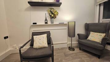 Una sala moderna con un sillón gris, un sofá, una lámpara de pie y un estante con objetos decorativos.