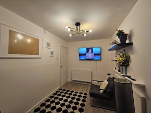 A modern living room with a black and white patterned rug, a black sofa, a TV mounted on the wall, and a ceiling light fixture. - Charming 2-bedroom Apartment in Deptford, Greater London, Near Greenwich (London)