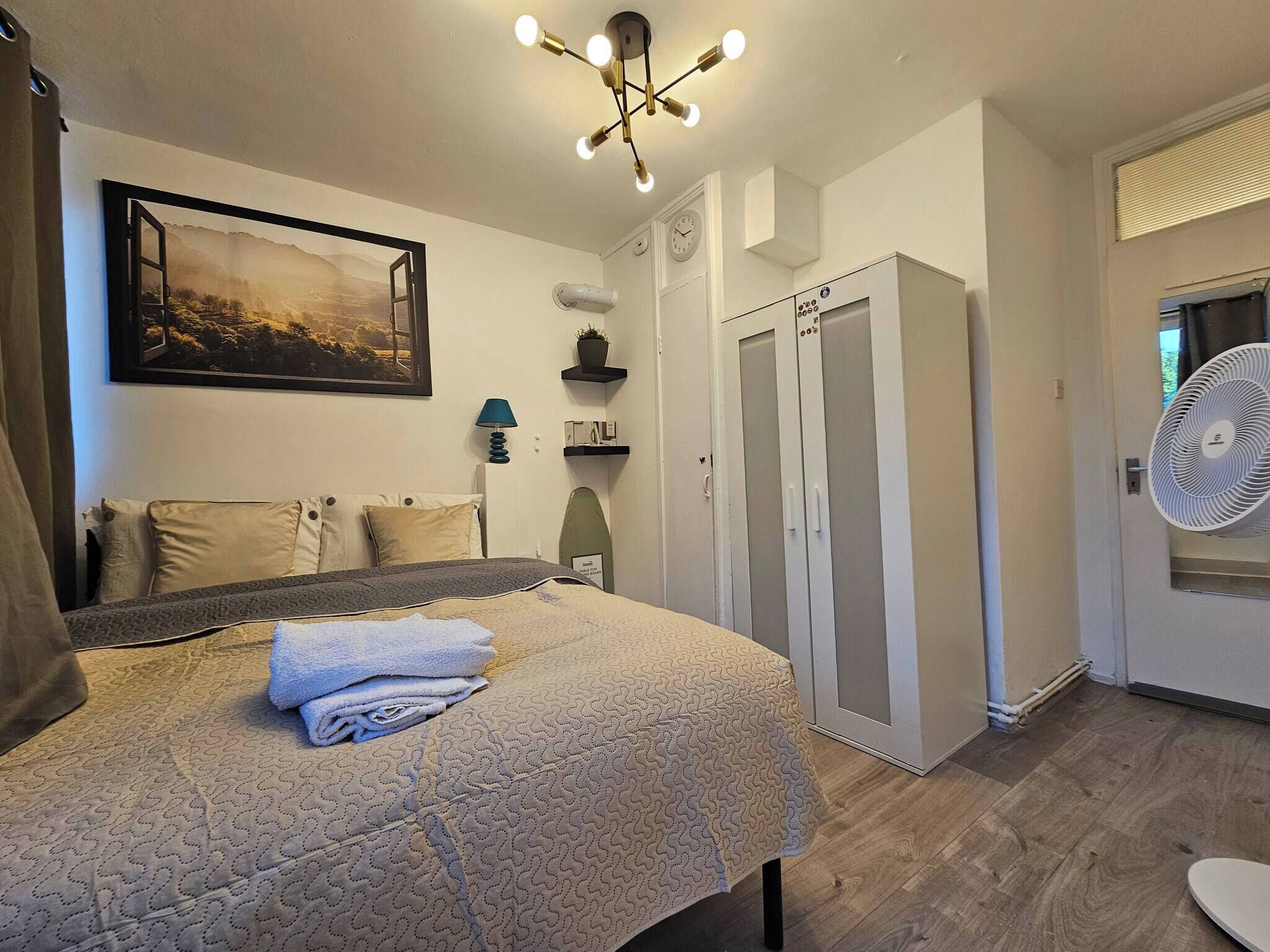 A bedroom with a bed, a wall-mounted picture, a ceiling light fixture, a wardrobe, and a fan.