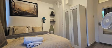 A bedroom with a bed, a wall-mounted picture, a ceiling light fixture, a wardrobe, and a fan.