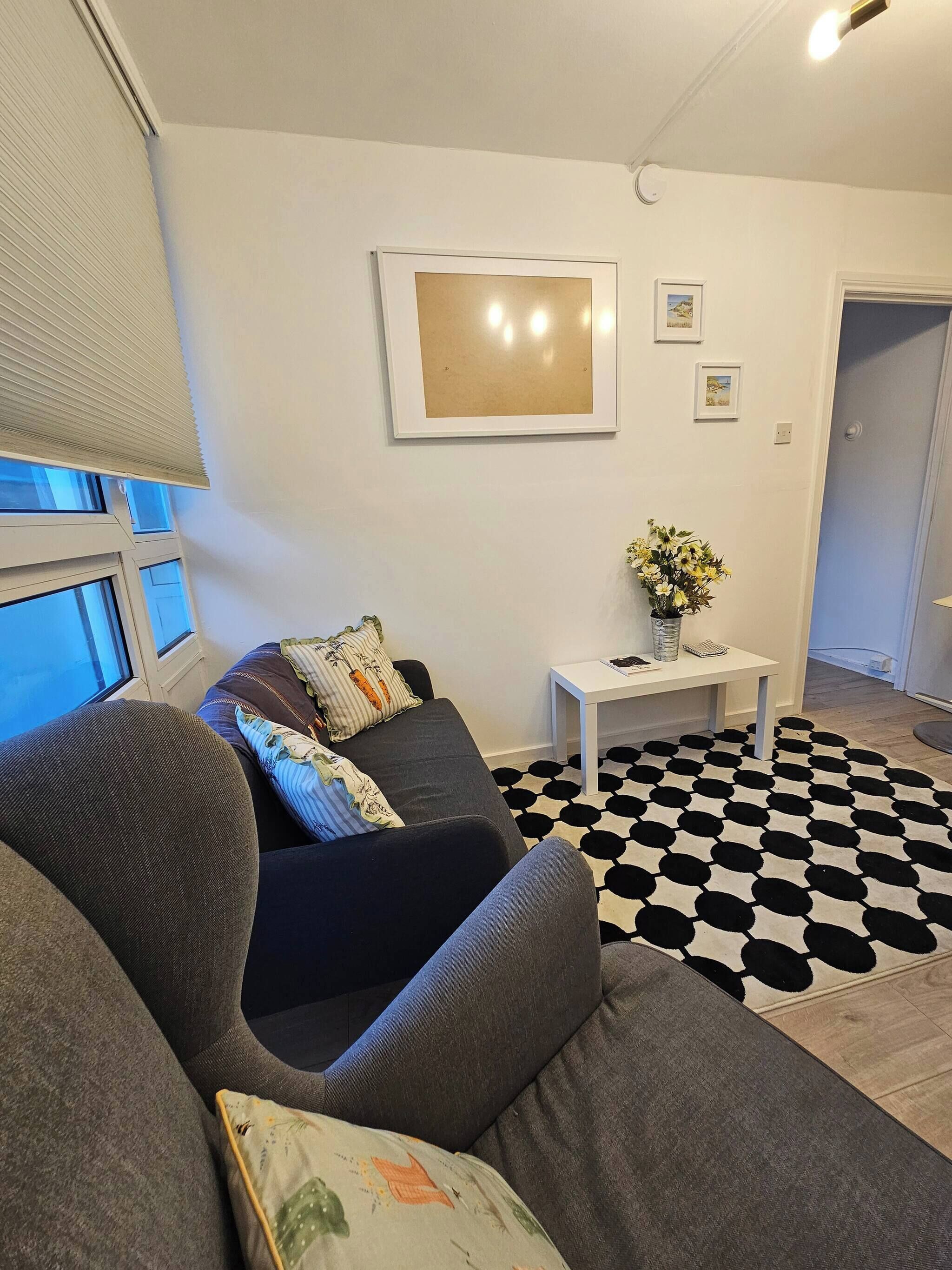 A living room with a grey sofa, a black and white patterned rug, and a small white side table with a vase of flowers.