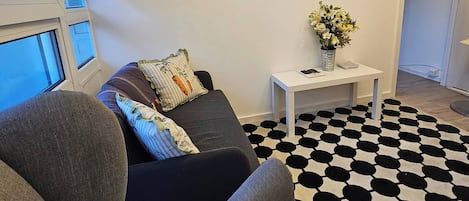 Una sala de estar con un sofá gris, un tapete estampado en blanco y negro, y una pequeña mesita auxiliar con un florero.