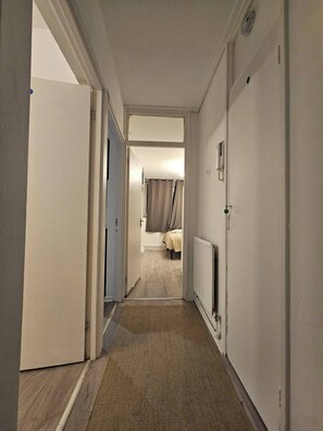 A narrow hallway leading to a bedroom with a bed, a radiator, and a door on the left. - Charming 2-bedroom Apartment in Deptford, Greater London, Near Greenwich (London)