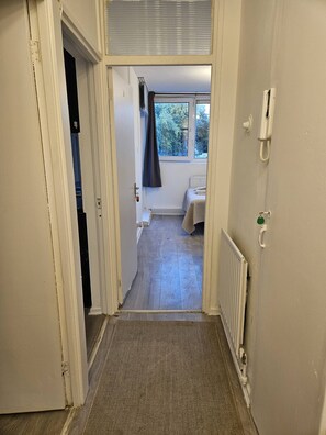 Ein schmaler Flur führt zu einem Schlafzimmer mit Fenster, Heizkörper und Telefon.