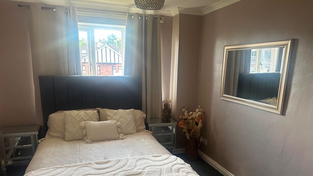 A bedroom with a bed, a nightstand, a mirror, and a window with curtains. - Apartment Sleeps 3 With Parking (Motherwell)