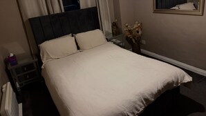 A neatly made bed with a headboard, a bedside table with a lamp, a vase with flowers, and a mirror on the wall. - Apartment Sleeps 3 With Parking (Motherwell)