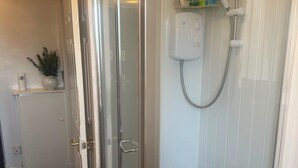 A glass-enclosed shower with a handheld showerhead, a white tiled wall, and a small shelf with toiletries. - Apartment Sleeps 3 With Parking (Motherwell)