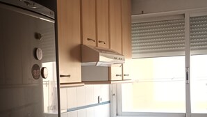 A kitchen with wooden cabinets, a stainless steel refrigerator, a built-in oven, and a window with blinds.