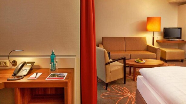 Habitación de hotel con cama, escritorio con teléfono, una silla, una mesita con fruta y televisor sobre un mueble.