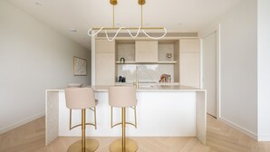 Una cocina moderna con una isla central, dos taburetes de bar y una lámpara colgante.