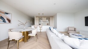 A modern living room with a round dining table, white sofas, and a kitchen area in the background. - Dromana Beach Suites - 101 (Dromana)