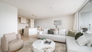 A modern living room with a sofa, a coffee table, and a chair. There is a kitchen area with a dining table and chairs. - Dromana Beach Suites - 102 (Dromana)