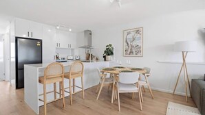A modern kitchen with white cabinetry, a black refrigerator, and a dining area with a round table and chairs. - Breakaway Beachside l Pool, 150mtrs to Beach (Maroochydore)