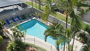 A swimming pool with lounge chairs, surrounded by palm trees and a white fence. - Breakaway Beachside l Pool, 150mtrs to Beach (Maroochydore)