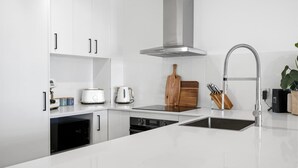A modern kitchen with white cabinetry, a stainless steel range hood, a double sink, and a built-in dishwasher. - Breakaway Beachside l Pool, 150mtrs to Beach (Maroochydore)