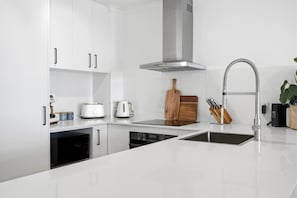 A modern kitchen with white cabinetry, a stainless steel range hood, a double sink, and a built-in dishwasher. - Breakaway Beachside l Pool, 150mtrs to Beach (Maroochydore)
