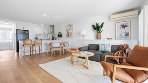 A modern living room with a sofa, coffee table, and chairs. There is a kitchen area with cabinets and a refrigerator. - Breakaway Beachside l Pool, 150mtrs to Beach (Maroochydore)