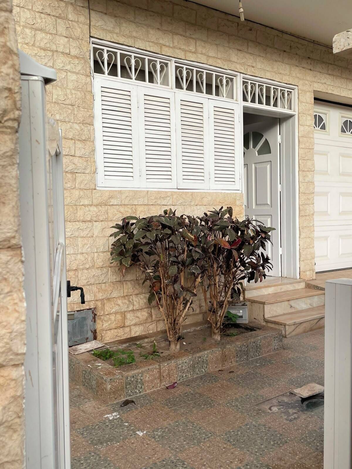 A house with a stone facade, white shutters, a garage door, and a small garden with plants.