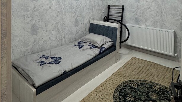 Ein Schlafzimmer mit einem Bett, einem Heizkörper, einer Deckenleuchte und einem gemusterten Teppich.