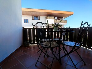 Ein Balkon mit gefliestem Boden, Metallstühlen, einem kleinen Tisch und einem Blumentopf.