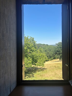 A room with an open door leading to a view of a forested landscape. - La Cerisaie - A house in the Nord/Aveyron region near Aubrac, Laguiole, and the Lot Valley. (Lassouts)