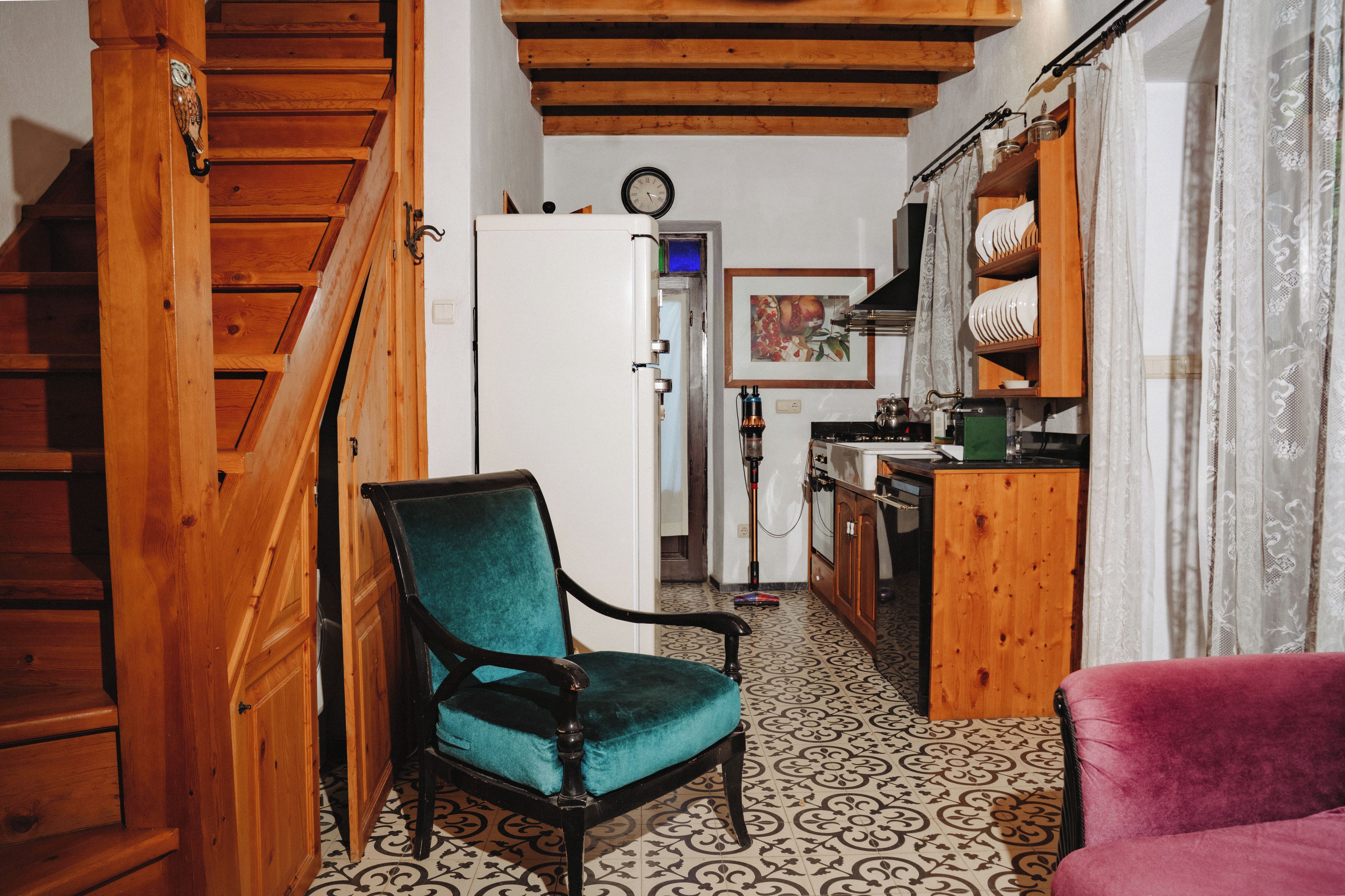 Een houten trap die leidt naar een kamer met een blauwgroene stoel, een kitchenette en een eethoek.