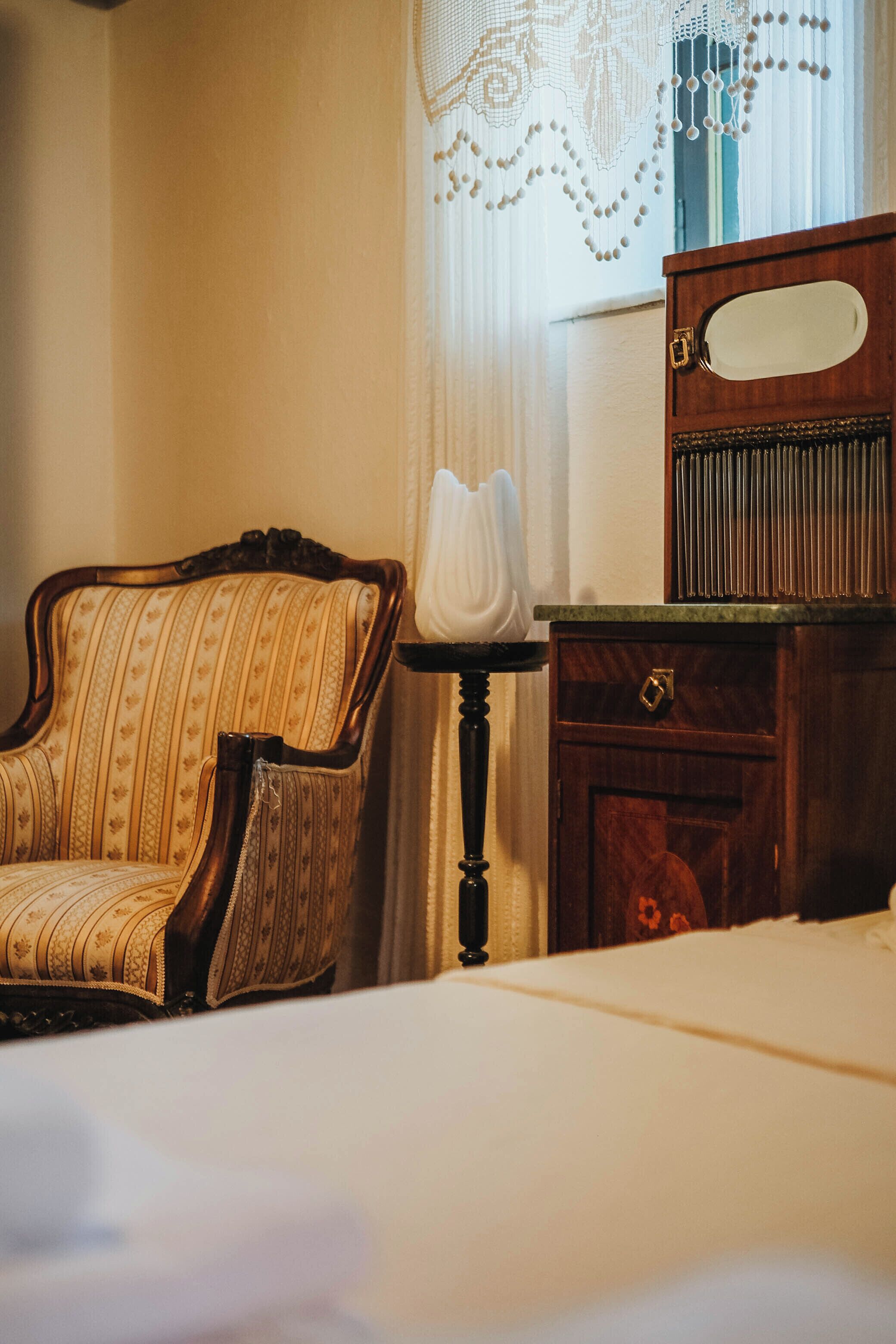 Une pièce comprenant un lit, une commode en bois, une chaise et une fenêtre avec des rideaux.