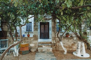 Edificio de piedra con puerta de madera oscura, escalones que conducen a la entrada y un pequeño jardín con plantas en macetas y una escultura blanca.