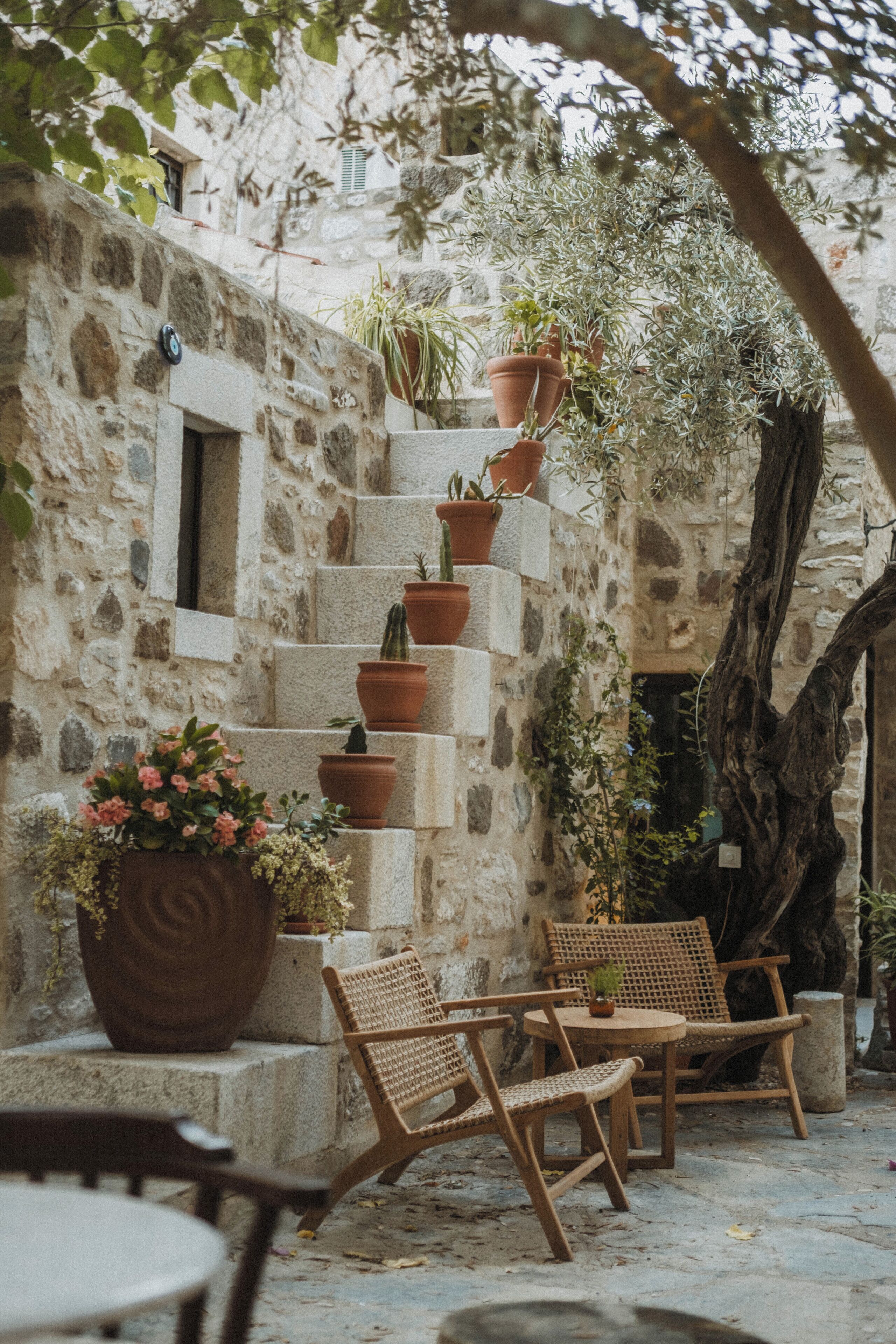 Un edificio de piedra con una escalera, plantas en macetas y mobiliario de mimbre.