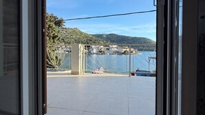 Uitzicht door een schuifdeur op een balkon, met een helder zicht op een wateroppervlak, een brug en een glooiend landschap.
