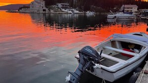 Een jachthaven met aangemeerde boten, een zonsondergang op de achtergrond en gebouwen aan de kust.